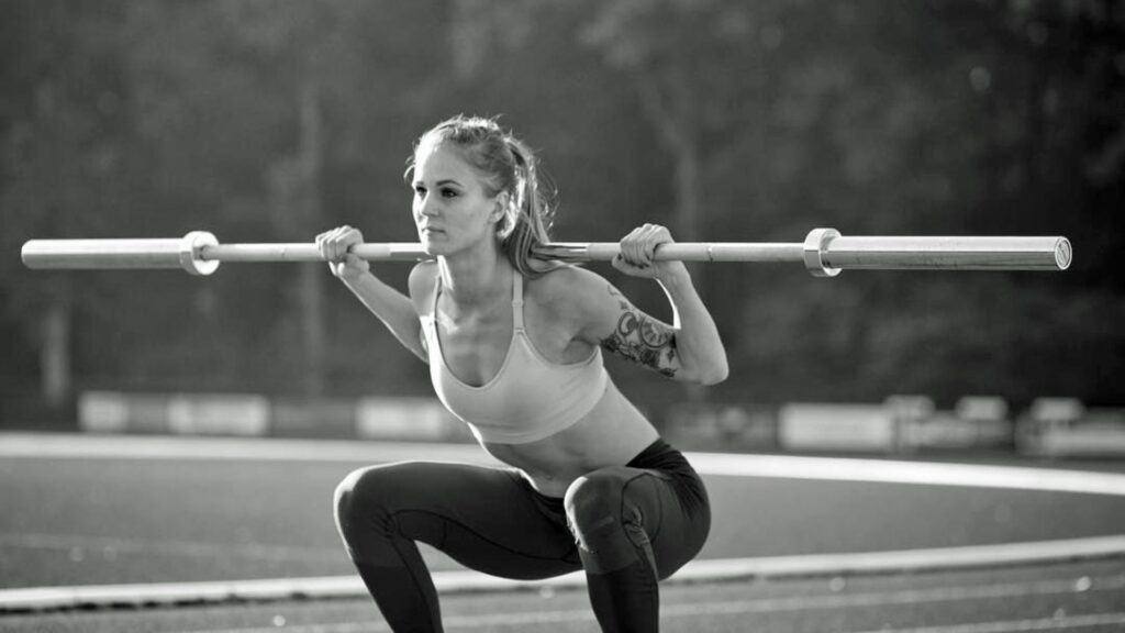 Black-and-white image of Elin Westerlund in a focused squat position with a barbell on her shoulders, outdoors on a training track.