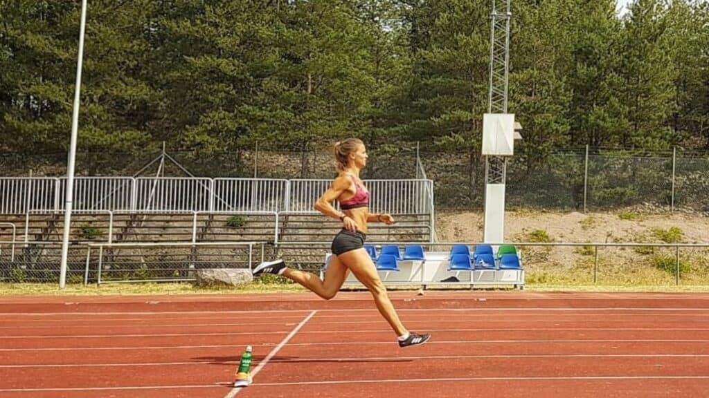 Swedish sprinter Elin Westerlund running on a track during a training session, with bleachers and trees in the background.