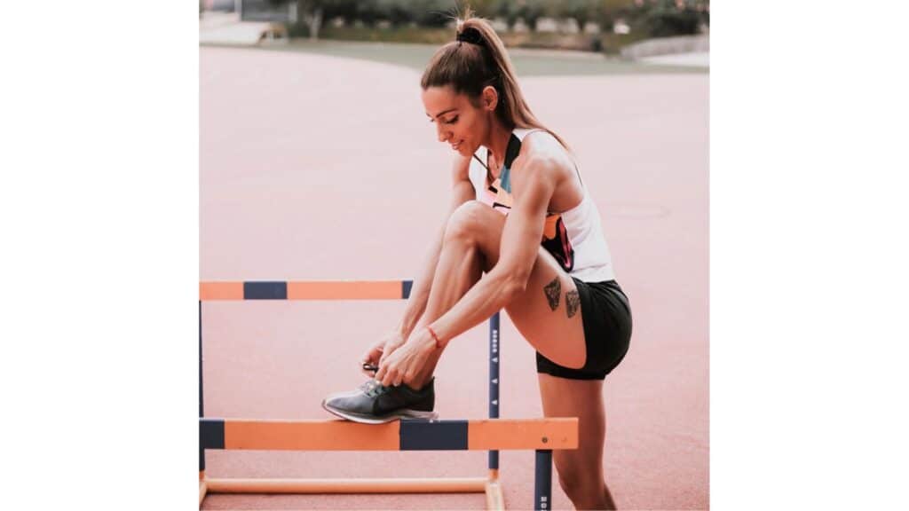 Ivet Lalova-Collio tying her running shoes while seated on a track hurdle, preparing for training with focus and determination.