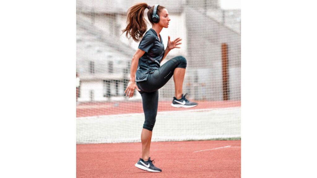 Bulgarian sprinter Ivet Lalova-Collio performing high knee drills on a track, wearing headphones and sportswear during a training session.