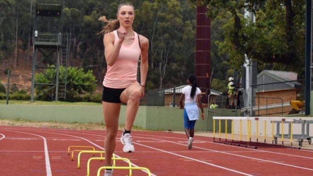 Laura Müller performing hurdle drills on a red track, focusing on form and movement during training, with trees in the background.